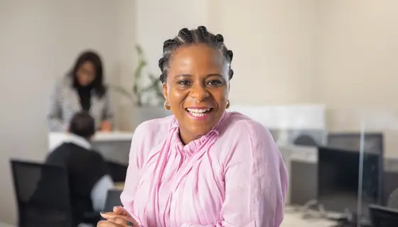 Portrait of Babalwa Damane, Director, Mining and Metals, South Africa sitting in office space in pink shirt smiling.