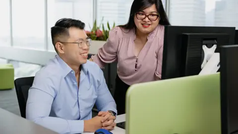 Male and female colleagues gathered around desk staring at computer screen.